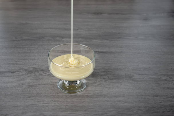 mleko skondensowane w szklanej miseczce na drewnianym tle - Zdjęcie, obraz