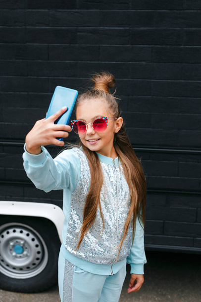 Pretty little girl in sunglasses making a selfie using a smart phone and smiling outdoor - Foto, Bild