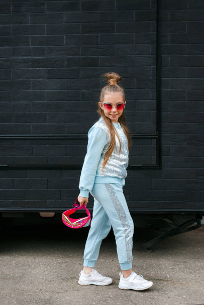 Little girl child wearing a sunglasses and backpack standing in over city background - Fotoğraf, Görsel