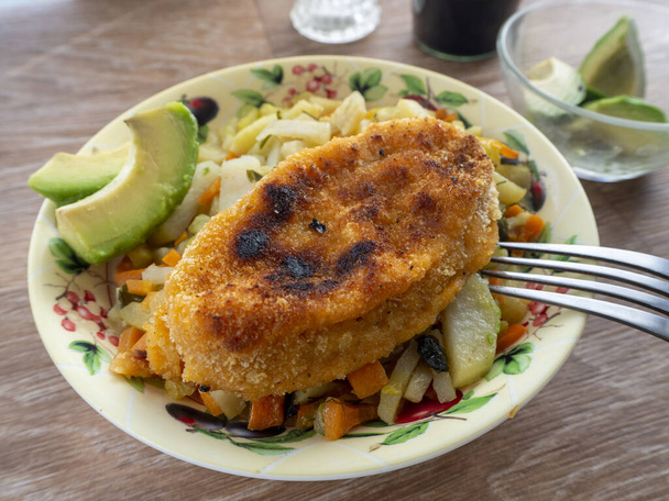 Gegrilde kotelet, gestoofde groenten en avocado voor de lunch. Een bord staat op een houten tafel. Achtergrond met zelfgemaakt eten. - Foto, afbeelding