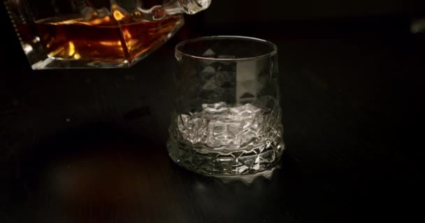 Slow motion golden whiskey pouring in the glass with ice cubes from the bottle. Close up V3 - Imágenes, Vídeo