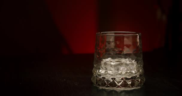 Slow motion golden whiskey pouring in the glass with ice cubes from the bottle on a red background. Close up - Imágenes, Vídeo