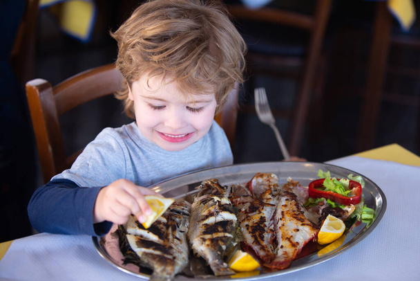 Λεμόνι για ψάρι. Αγόρι ρίχνει χυμό λεμονιού σε ψάρια στο εστιατόριο. Γεύμα στο παραθαλάσσιο καφέ. Θαλασσινά για μεσημεριανό γεύμα για παιδιά. Υπέροχο δείπνο.. - Φωτογραφία, εικόνα