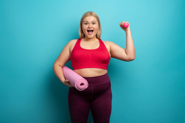 Fat girl does gym at home. satisfied expression. Cyan background - Photo, Image