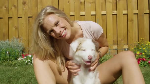 Movimiento lento: Chica rubia feliz acariciando a su perro en el patio trasero en un día soleado
. - Metraje, vídeo