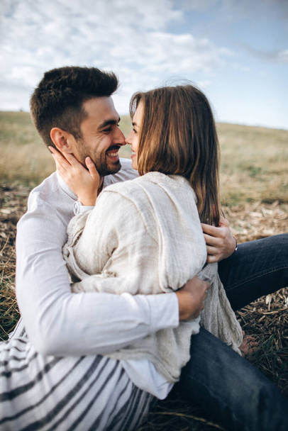 Bella coppia che abbraccia, bacia e sorride contro il cielo seduta sull'erba. Ritratto ravvicinato
 - Foto, immagini