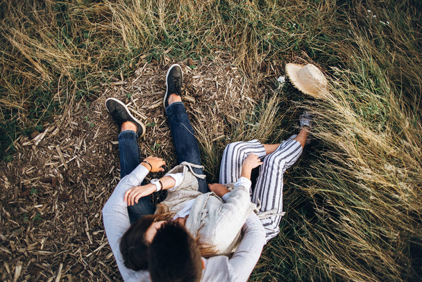 Прекрасная пара обнимается, целуется и улыбается на фоне неба, сидя на траве. Вид сверху
 - Фото, изображение