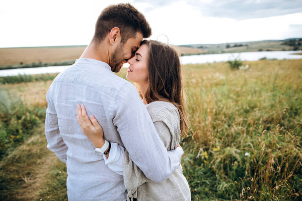 A boldog pár ölelkezik, csókolózik és mosolyog az égen a mezőn. Kalap a lány kezében. - Fotó, kép