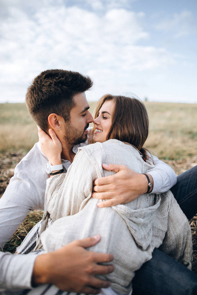 Preciosa pareja abrazándose, besándose y sonriendo contra el cielo sentado en la hierba. Retrato de primer plano
 - Foto, imagen