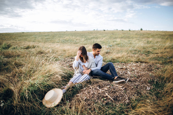 Lovely couple hugging, kissing and smiling against the sky seating on grass. Space for text - Foto, imagen