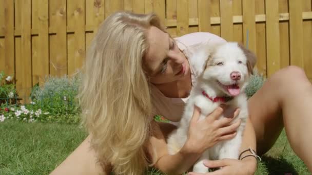 CERRAR: Chica sonriente besa al cachorro blanco esponjoso mientras juega en el patio - Metraje, vídeo