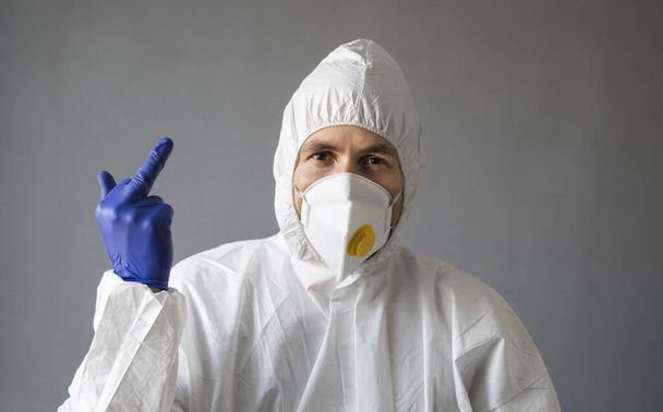 白い保護スーツの医師、医療用マスクとゴム手袋は、ウイルスに中指を示しています。人々を助ける一方、コロナウイルスのパンデミックの脅威。感染症、コロナウイルスのパンデミックは19. - 写真・画像