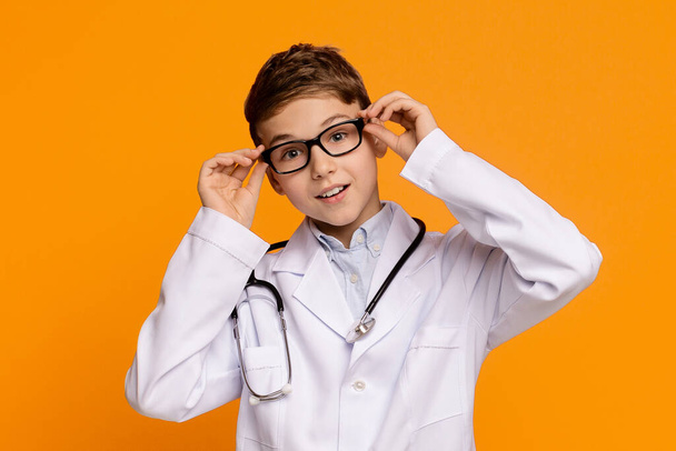 Playful teenager in medical uniform posing on orange background - Foto, afbeelding