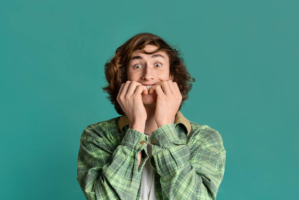 Curly teenager biting his nails in fear on color background - Photo, image