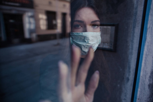 La mujer lleva una máscara debido a la contaminación del aire. Paciente aislado para prevenir la infección durante la Cuarentena. Coronavirus. Mujer enferma de covid-19 mirando por la ventana y usando protección antifaz
.  - Foto, Imagen