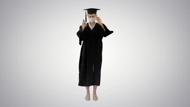 Φοιτητής αποφοίτησης με ιατρική μάσκα χρησιμοποιώντας απολυμαντικό σε βαθμιδωτό φόντο. - Πλάνα, βίντεο