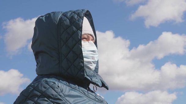 Пандемия коронавируса. Пожилая женщина на улице в медицинской маске и капюшоне. женщина носит защитные маски на улице. концепция здоровья, карантин коронавируса N1H1, защита от вирусов. опасная инфекция
 - Фото, изображение