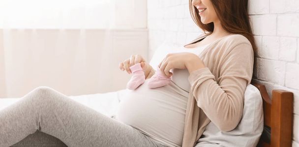 Mulher grávida brincando com pequenas botas e sua barriga
 - Foto, Imagem
