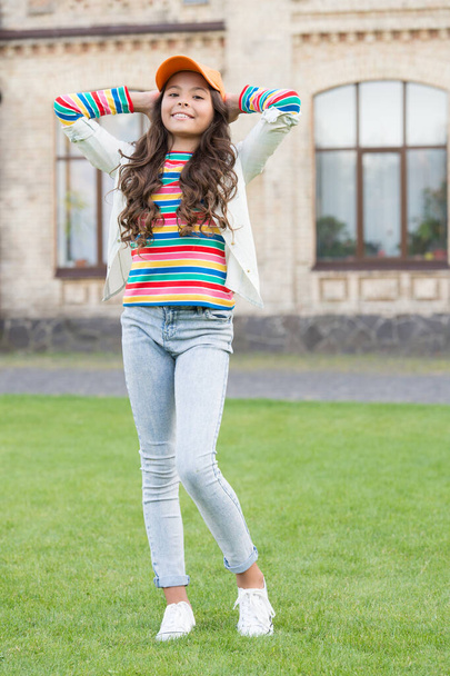 pretty brunette child in street. spring fashion and beauty. happy childrens day. stylish kid in cap. warm and friendly smile. concept of healthy lifestyle. cute little girl has curly hair - Zdjęcie, obraz