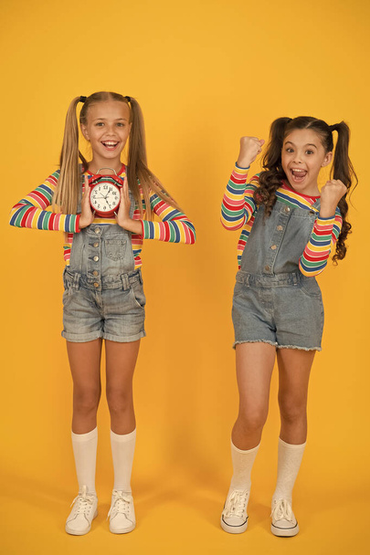 two happy girls hold alarm clock. back to school. summertime. discipline and time management. teenage girls yellow wall. children vintage clock. counting for lunch time. children break concept - Foto, afbeelding