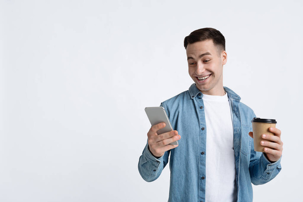 Guy κοιτάζει smartphone, κρατώντας κύπελλο - Φωτογραφία, εικόνα