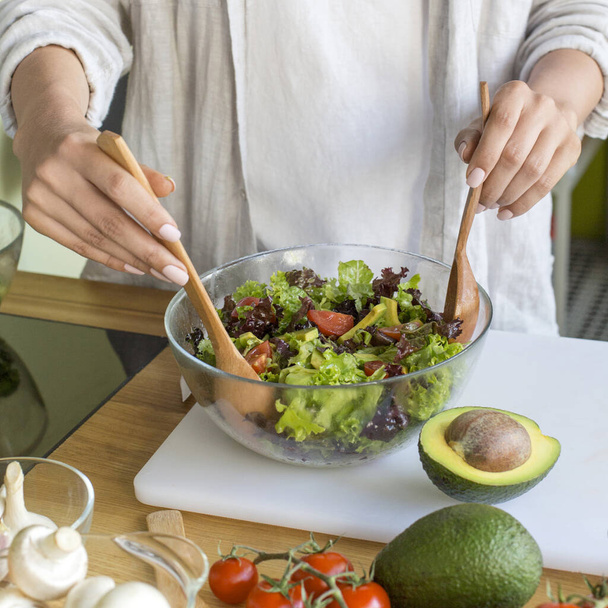 Young unrecognizable woman preparing vegetable salad with avocado - Foto, imagen