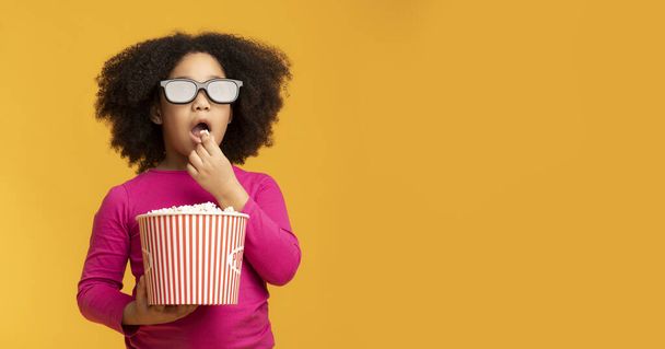 Cine infantil. Niña negra usando gafas 3D y comiendo palomitas de maíz
 - Foto, imagen