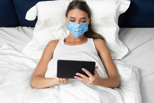 Vrouw in het gezicht masker met behulp van tablet liggend in bed Indoor - Foto, afbeelding