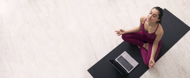 Сиди дома. Девушка тысячелетия в йоге лотоса позирует, слушая онлайн медитацию на ноутбуке, панораму. Вид сверху
 - Фото, изображение