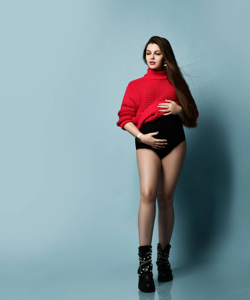 Beautiful pregnant girl in a red sweater holds her belly pregnancy, motherhood, people and expectation concept - Foto, Imagen