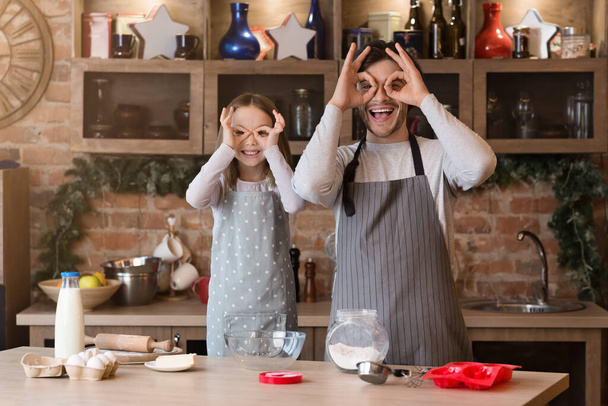 schattig klein meisje en haar vrolijke vader het hebben van plezier in keuken - Foto, afbeelding