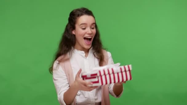 Adorable teenage brunette girl taking long-awaited present for her birthday and jumping smiling shouting excitedly, rejoicing nice gift, celebrating holidays. studio shot isolated on green background - Video