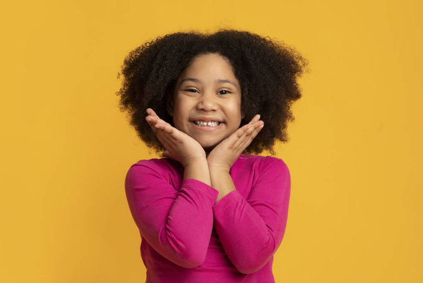 Портрет радостной маленькой черной девочки, трогающей лицо от волнения
 - Фото, изображение