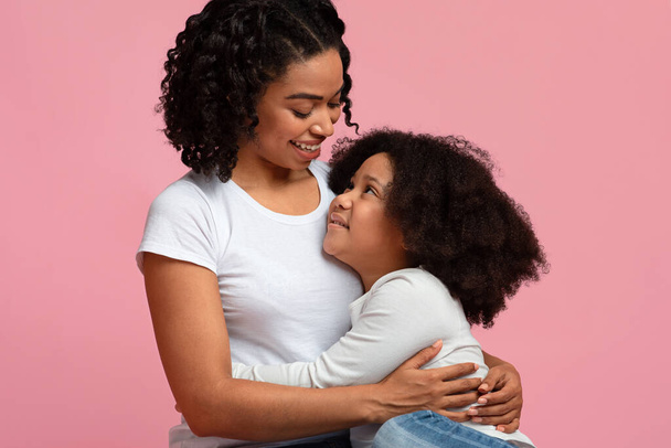 Moeder en dochter connectie. glimlachende zwarte vrouw omarmen klein meisje - Foto, afbeelding