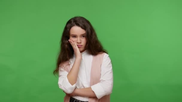 Pensive cute teen brunette girl in white shirt having smart thought, pondering idea or difficult question, looking dissatisfied having doubts about choice. studio shot isolated on green background - Πλάνα, βίντεο