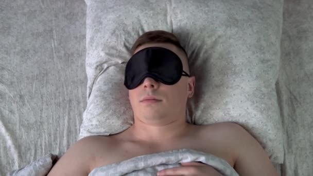Un giovane non può addormentarsi con una maschera del sonno. Un uomo giace a letto nella sua stanza e soffre di insonnia. Vista dall'alto
. - Filmati, video