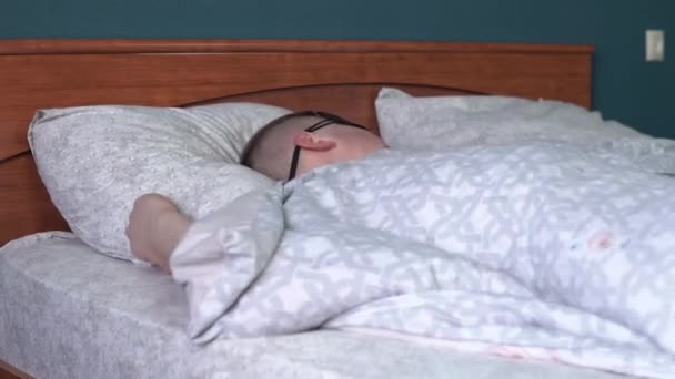 若い男は睡眠マスクで眠りに落ちることはできません。男は自分の部屋にベッドに横たわって不眠症に苦しんでいます. - 映像、動画