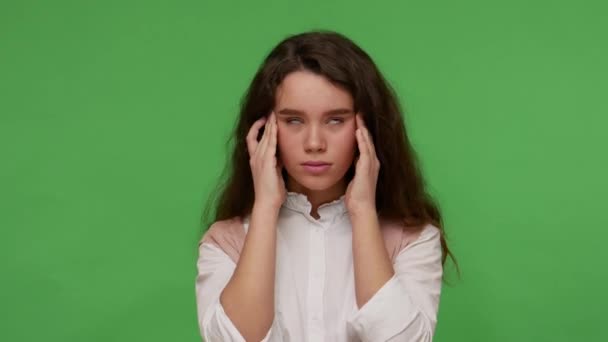 Sick teenage brunette girl in white shirt rubbing her temples, suffering headache, migraine in adolescence, experiencing stress and depression, flu fever. studio shot isolated on green background - Video, Çekim