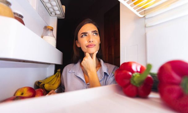 Gedachte huisvrouw kijkt in de koelkast, uitzicht van binnenuit - Foto, afbeelding