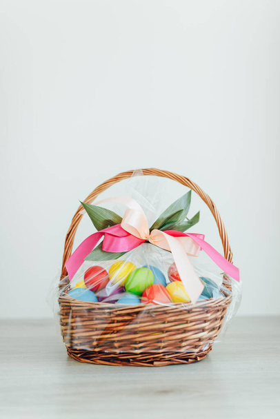 Easter color eggs in festive gift basket, light gray wooden background with copy-space - Foto, Imagen