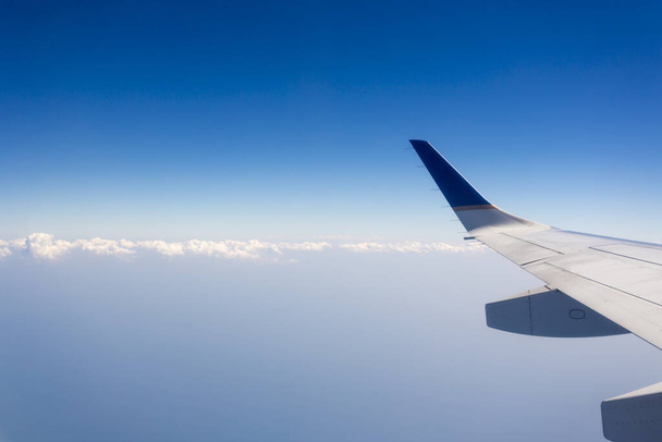 View of jet plane wing with crystal blue sky in the background and clouds with copy space. - Foto, afbeelding