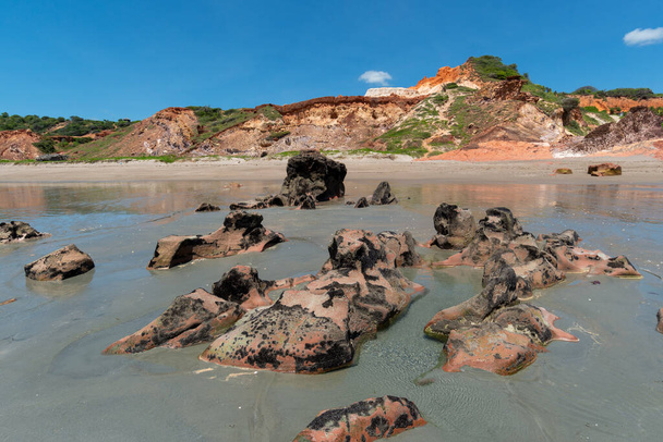 Piedras de colores y arena en la playa, en los acantilados de fondo con vegetación natural en Praia de Peroba, Icapui, Ceara, Brasil en abril 23, 2016
 - Foto, imagen