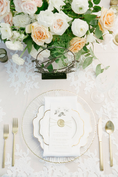 Una mesa de cena sentada para una persona, ensamblada con una tarjeta de menú, porcelana blanca y dorada, utensilios de oro y flores recién cortadas a lo largo de un número de mesa
 - Foto, imagen