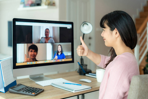 アジアのビジネス女性はビデオ会議の計画について彼女の同僚に親指を立てる。ビデオ通話でオンライン会議のためにコンピュータを使用して多民族のビジネスチーム。家で働くスマートなグループ. - 写真・画像