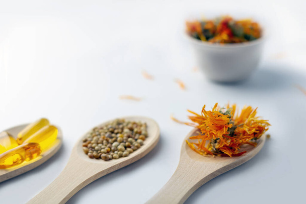 Herbal capsule, natural vitamins, dry calendula flowers at wooden spoon on white background. Concept of healthcare and alternative medicine: homeopathy and naturopathy. Close up, copy space for text - Φωτογραφία, εικόνα