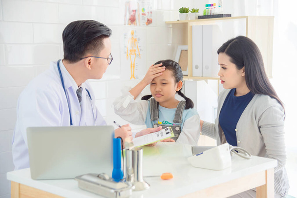 Joven chica asiática con dolor de cabeza y fiebre vienen a visitar al médico con su madre en la clínica médica. - Foto, Imagen