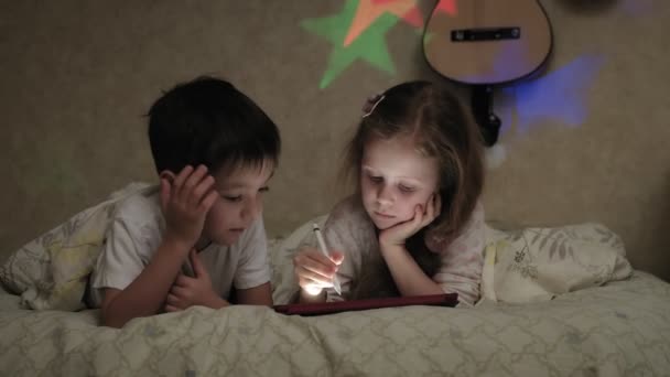 I bambini piccoli, fratello e sorella sono sdraiati sul letto e giocano sul tablet prima di andare a letto
. - Filmati, video