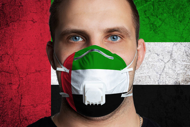 Young man with sore eyes in a medical mask painted in the colors of the national flag of United Arab Emirates. Coronovirus disease  COVID-19 concept.  Man is afraid of getting the flu - Photo, Image
