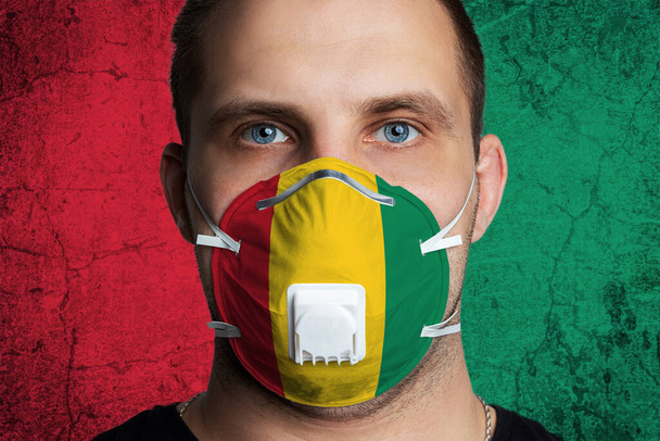 Young man with sore eyes in a medical mask painted in the colors of the national flag of Guinea. Coronovirus disease  COVID-19 concept.  Man is afraid of getting the flu - Photo, Image