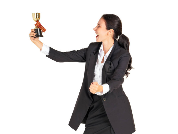 Una mujer de negocios con un traje negro con una sonrisa mirando el trofeo recibido del trabajo realizado con orgullo. Retrato sobre fondo blanco con luz de estudio
. - Foto, Imagen
